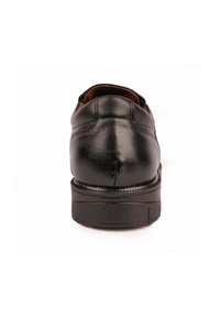 Zapatos de cuero negro con una textura suave, punta redondeada y suela de goma gruesa y baja. Presentan costuras a lo largo de la parte trasera y un interior acolchado.