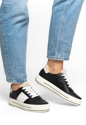 Czarne teksturowane sneakersy z białymi skórzanymi akcentami, beżowym zamszowym kołnierzem, białymi sznurowadłami i grubymi gumowymi podeszwami. Widoczne jasnoniebieskie dżinsy.