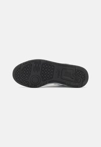 Semelle de chaussure de sport noire avec une adhérence en caoutchouc texturé et un motif hexagonal. Elle présente un bout arrondi et un talon renforcé pour la stabilité.