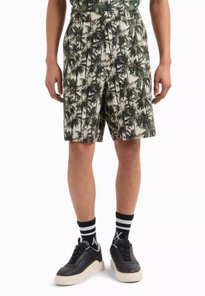 Șorturi bărbătești cu un model cu palmieri, în culori bej și verde închis, design pliat și talie elastică, asortate cu adidași negri și șosete cu dungi.