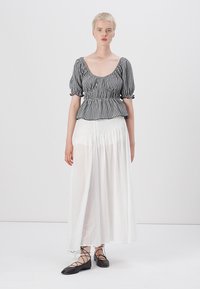 Top peplum in bianco e nero a scacchi con maniche a sbuffo, abbinato a una gonna maxi bianca fluente. Ballerine nere con lacci.