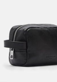 Bolso de viaje de cuero negro con forma rectangular, cierre de cremallera y un asa lateral. Presenta un logo sutil y una textura suave.