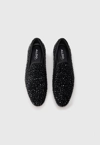 Black slip-on shoes decorated with clustered shiny black beads, viewed from above on a plain white background.