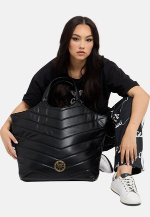Sort quiltet håndtaske med chevronmønster, fremstillet af skinnende materiale. Har en rund guldfarvet detalje foran og solide håndtag.