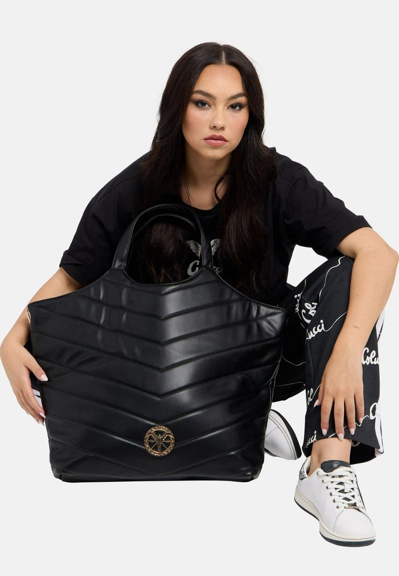 Schwarze gesteppte Handtasche mit Chevron-Muster, aus glänzendem Material gefertigt. Verfügt über ein kreisförmiges goldfarbenes Hardware-Detail an der Vorderseite und robuste Griffe.