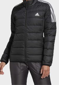 Černá péřová bunda s horizontálním prošíváním, vysokým límcem, plným zipem a bílými třemi pruhy na ramenech. Obsahuje logo Adidas.