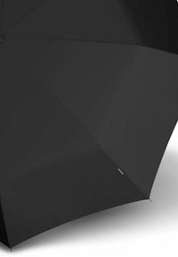 Zwarte paraplu geopend, met meerdere stoffen panelen en een klein label dicht bij een rand, geplaatst tegen een effen witte achtergrond.