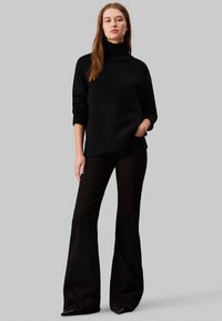 Svart, överdimensionerad turtlenecksweater med ribbat mönster, tillsammans med svarta utsvängda byxor. Slätt tyg och åtsittande ärmar framhäver outfiten.