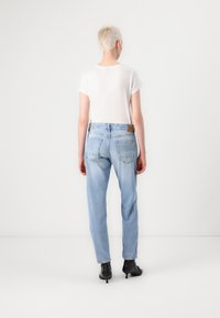 Lichtblauwe denim jeans met een relaxed fit, vijf zakken ontwerp en een bruine leren patch op de tailleband, aangevuld met een wit T-shirt.