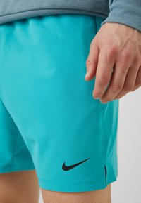 Nike türkiissinised lühikesed püksid vertikaalse soonte tekstuuriga. Asetatud must Swoosh logo ja külgedel lõhed liikumise lihtsustamiseks.