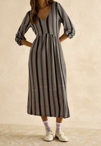 Vestido midi a rayas en blanco y negro con escote en V y mangas tres cuartos, que presenta una cintura fruncida y una tela texturizada.
