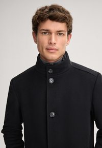 Cappotto in misto lana nero con colletto alto, dotato di quattro bottoni, design slanciato e tessuto texturizzato. Nessun motivo o dettaglio visibile.