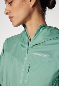 Lightweight mint green zip-up jacket with a hood, featuring a nylon texture and embroidered logo. Zipper toggle in matching color.