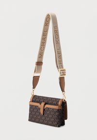 Ruskeakuvioinen käsilaukku beigen sävyisillä yksityiskohdilla ja irrotettavalla hihnalla, jossa on merkin nimi. Laukussa on etumäinen läppä ja kullanväriset metalliosat.