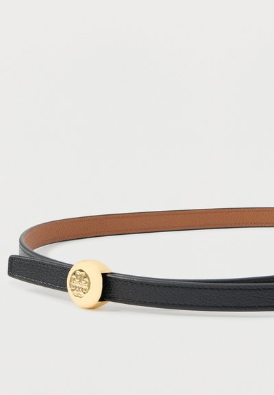 Čierny kožený opasok s textúrovaným povrchom, vybavený okrúhlym zlatým emblémom ako prackou. Vnútorná strana je hladká hnedá koža.