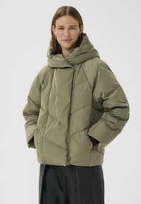 Giubbotto imbottito verde oliva con colletto alto, trapuntatura a rombi e tasche laterali. Il materiale appare liscio con una leggera lucentezza.