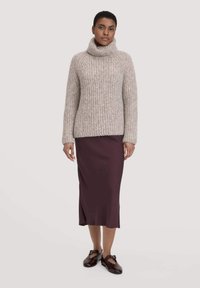 Beige gestrickter Rollkragenpullover mit gerippter Textur, kombiniert mit einem taillierten burgunderfarbenen Midikleid und dunkelbraunen Slippern.