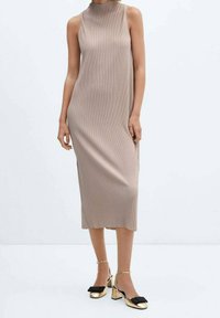 Vestido midi de canalé beige con un escote alto. Combina con zapatos de tacón bloque dorados que tienen un lazo negro como detalle. Textura suave.