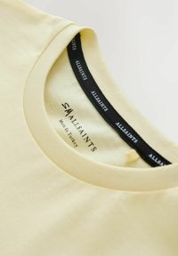 Svetložltý bavlnený golier trička s označením značky AllSaints a veľkosťou Small vytlačenou vo vnútri, vyrobený v Turecku.