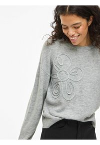 Grijze gebreide trui met een opvallend geborduurd bloemmotief in een lichtere tint. Heeft een ronde hals en een losse pasvorm.