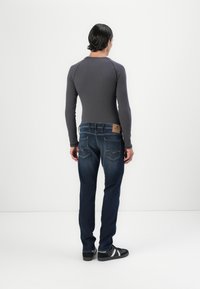 Haut gris à manches longues avec une texture côtelée, associé à un jean bleu foncé portant une pièce en cuir et un design de couture sur la poche arrière.