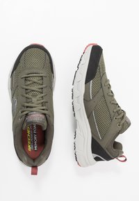 Zapatillas deportivas verde olivo con paneles de malla, suelas de goma y acentos negros. Cuentan con una plantilla de espuma viscoelástica y una lengüeta en la parte trasera para facilitar su uso.