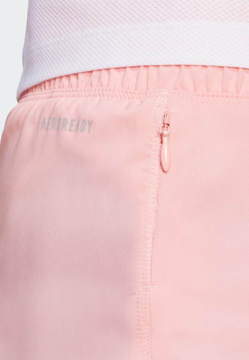 Helle pinkfarbene Sportshorts aus glattem Material, mit einem elastischen Taillenbund und einer Reißverschlusstasche mit einem weißen "AEROREADY"-Logo.