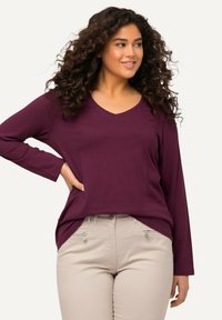 Burgundské tričko s dlouhým rukávem a V výstřihem vyrobené z měkké látky, spárované se světle béžovými kalhotami s zipovými kapsami a přiléhavým střihem.