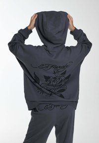 Sudadera gris con un bolsillo frontal, con un gran diseño gráfico negro y texto en la parte posterior. Material de algodón suave con un corte holgado.