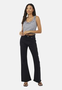 Jean noir évasé associé à un haut cropped à carreaux noir et blanc avec un col volanté. Le mannequin porte des sandales noires à lanières.