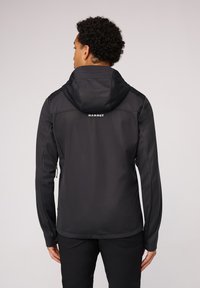 Zwarte softshell jas met capuchon, voorzien van een gladde textuur, ritszakken aan de zijkant en een logo tekst op de achterkant.