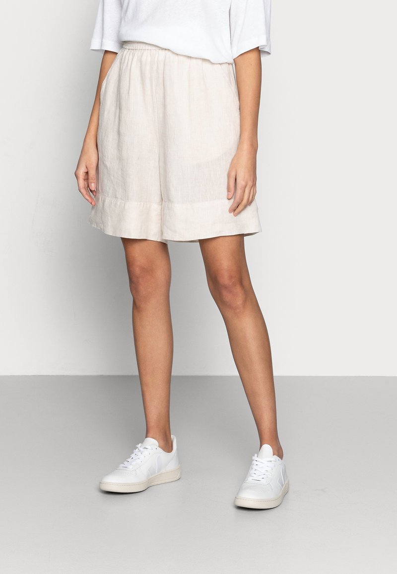 Pantaloni beige in lino con una vestibilità rilassata, cintura elastica arricciata e tasche laterali. Abbinati a sneaker bianche per un look casual.