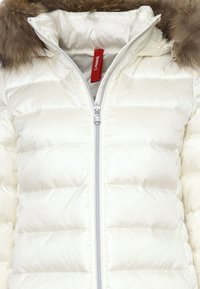 Giacca puffer crema con cappuccio foderato in pelliccia, con zip frontale completa e texture trapuntata. Include un'etichetta rossa del marchio sul collo.