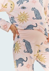 Ljust rosa pyjamasset med ett mönster av leoparder, solar och himmelska designer; tillverkat av mjukt tyg med avslappnad passform och rynkad detalj vid midjan.