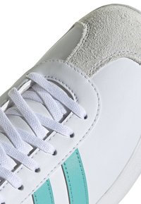 Vit sneaker med mintgröna ränder, i läder och mocka, platta vita snören och en design med rundad tå. Slät textur med sömnadsdetaljer.