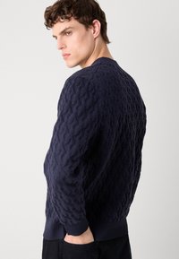 Granatowy sweter z dzianiny o teksturowanym wzorze. Posiada ściągacze przy mankietach i u dołu, okrągły dekolt oraz dopasowany krój.