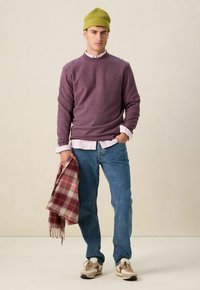 Paarse sweatshirt, witte collared shirt eronder, blauwe denim jeans, beige en rode geruite sjaal, groene gebreide beanie en lichte sneakers.