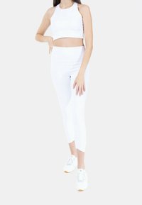 Valkoinen urheilu crop top ja legginsit venytyskankaasta; tiukka malli, saumaton viimeistely, yhdistetty valkoisten urheilukenkien kanssa, joissa on oranssia korostusta.