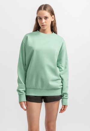 Mint green sweatshirt made of soft fabric, featuring a round neck, long sleeves, and a relaxed fit. Paired with black shorts.