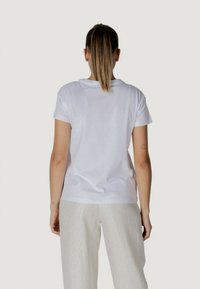 T-shirt bianco a maniche corte con scollo rotondo, texture liscia, vestibilità leggermente rilassata, abbinato a pantaloni chiari a fantasia.
