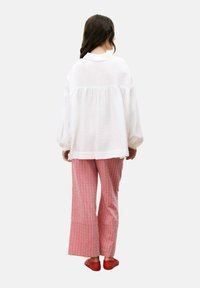 Witte, gestructureerde blouse met lange mouwen en een gathered taille, gecombineerd met roze gestreepte wijde broek en rode instappers.