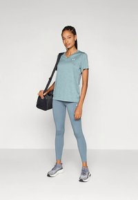 Svetlo modra atletska majica z V-izrezom, kombinirana z ujemajočimi se legicami. Temni supergi in črna torbica čez ramo. Gladek tekstura in sodoben kroj.