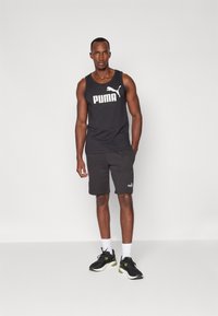 Herreidrettsantrekk bestående av en svart tank top med hvit "PUMA"-logo, grå shorts og svarte joggesko med grønne detaljer.
