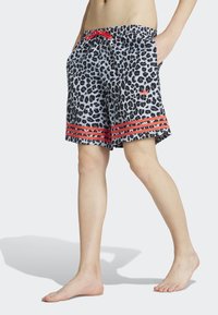 Sorte og hvide leopardmønstrede svøm shorts med en rød snor, sidelommer og røde vandrette striber i kanten.
