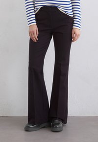 Czarne spodnie flare o gładkiej fakturze i dopasowanej talii, zestawione z niebieską i białą pasiastą bluzką z długim rękawem.