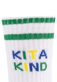 Biała bawełniana skarpeta z zielono-białym prążkowanym mankietem. Posiada napis "KITA KIND" w niebieskich, zielonych i żółtych literach na korpusie.