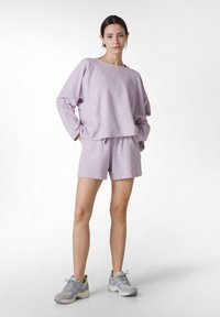 Lila lounge set bestående av en löst sittande långärmad topp och matchande shorts, tillverkad av mjukt tyg. Lätta sneakers fulländar looken.