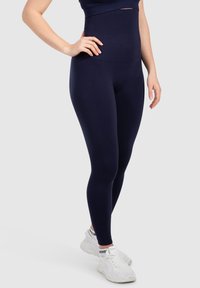 Leggings blu navy a vita alta realizzati in tessuto elasticizzato, caratterizzati da una superficie liscia e una silhouette aderente, abbinati a scarpe da ginnastica bianche.