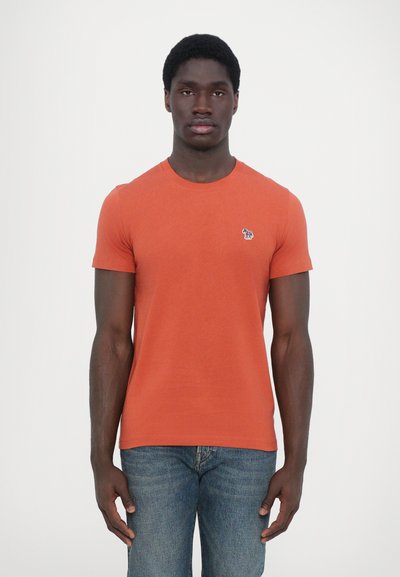 T-shirt orange à manches courtes en coton avec un col rond, portant un petit logo d'éléphant brodé sur la poitrine gauche.