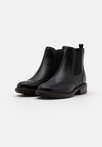 Botas de cuero negro hasta el tobillo con paneles laterales elásticos, detalles decorativos de brogue, un tacón bajo apilado y una lengüeta en la parte trasera.